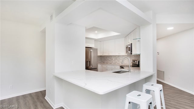 kitchen with light hardwood / wood-style flooring, tasteful backsplash, kitchen peninsula, white cabinets, and appliances with stainless steel finishes