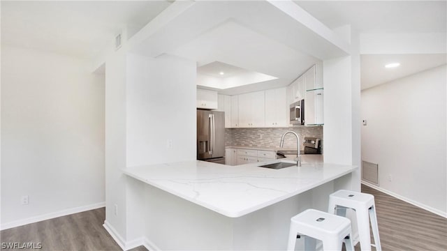 kitchen featuring sink, appliances with stainless steel finishes, white cabinetry, decorative backsplash, and kitchen peninsula