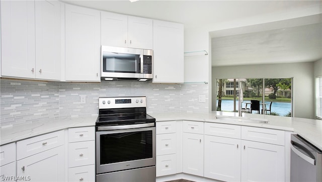 kitchen with decorative backsplash, light stone counters, stainless steel appliances, and white cabinets