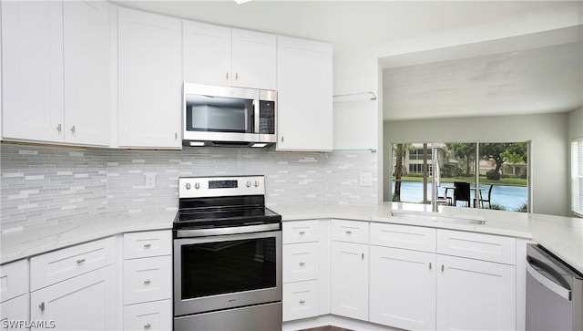 kitchen with stainless steel appliances, tasteful backsplash, white cabinets, and light stone counters