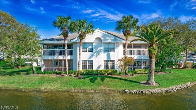 rear view of house with a balcony, a water view, and a lawn