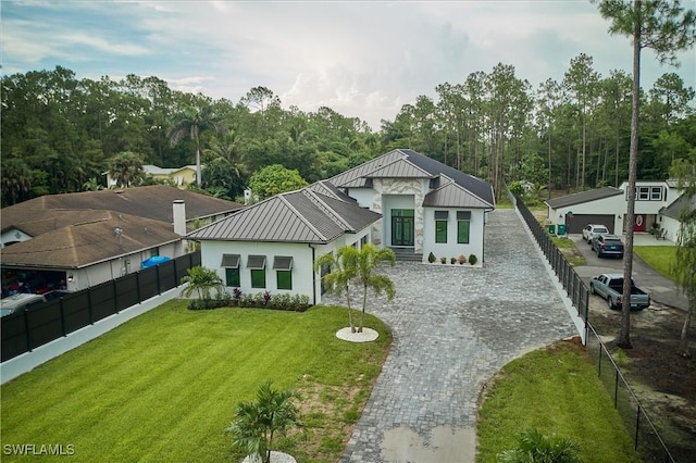 view of front facade featuring decorative driveway, a front yard, a standing seam roof, fence, and metal roof