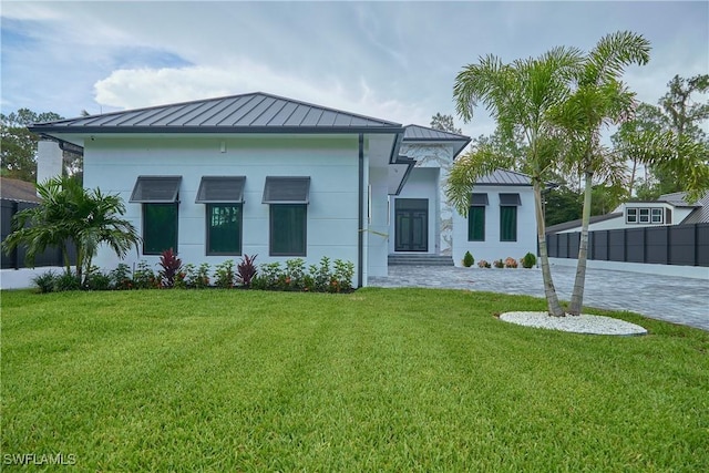 view of front facade with metal roof, a standing seam roof, decorative driveway, a front yard, and stucco siding