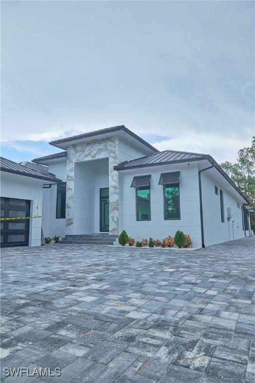 contemporary home with decorative driveway, a standing seam roof, and metal roof