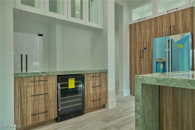 bar with a bar, wine cooler, high end refrigerator, and light wood-style floors