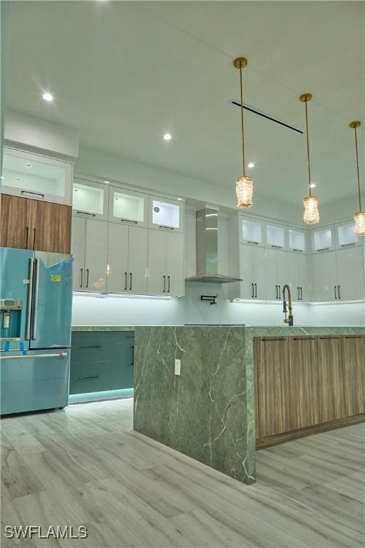 kitchen featuring light countertops, glass insert cabinets, white cabinetry, high quality fridge, and wall chimney exhaust hood