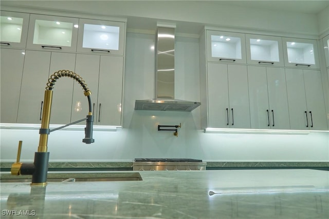 interior details featuring wall chimney exhaust hood, glass insert cabinets, and white cabinets