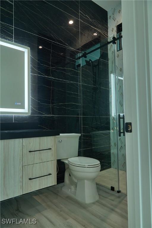 full bath with a marble finish shower, tile walls, toilet, and vanity