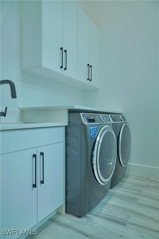 laundry area featuring cabinet space, baseboards, light wood finished floors, and washer and dryer