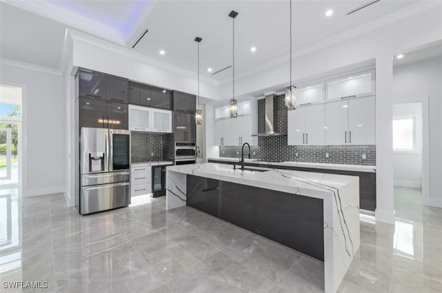 kitchen featuring sink, wall chimney range hood, pendant lighting, a center island with sink, and appliances with stainless steel finishes