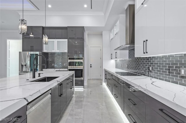 kitchen featuring white cabinets, wall chimney range hood, sink, appliances with stainless steel finishes, and decorative light fixtures