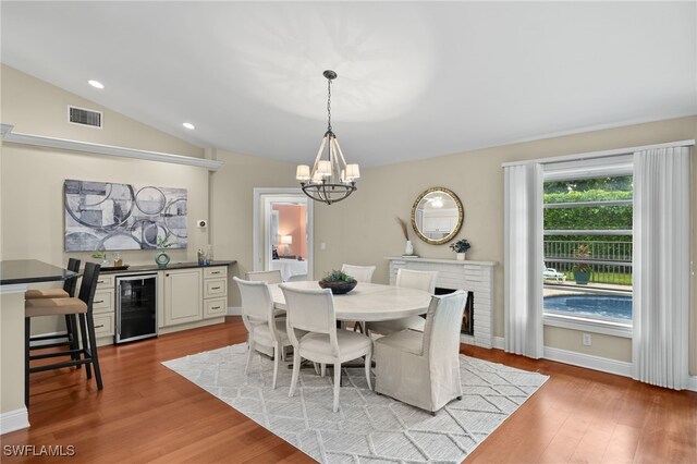 dining room featuring a notable chandelier, lofted ceiling, beverage cooler, and light hardwood / wood-style floors