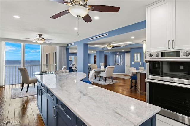 kitchen with blue cabinetry, a water view, white cabinets, dark hardwood / wood-style floors, and double oven