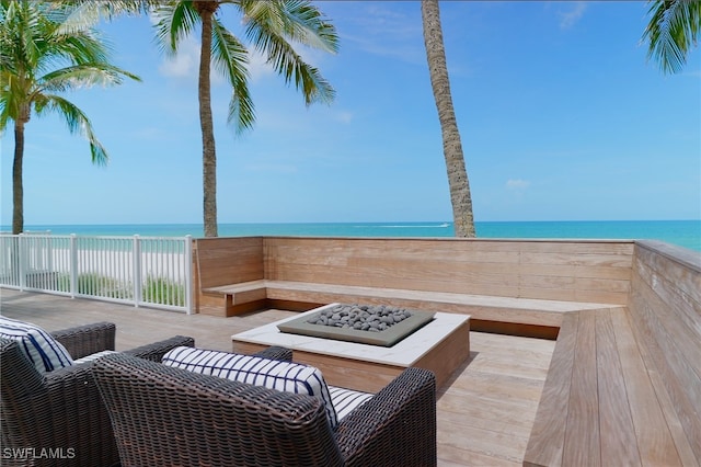 deck featuring an outdoor fire pit, a water view, and a beach view