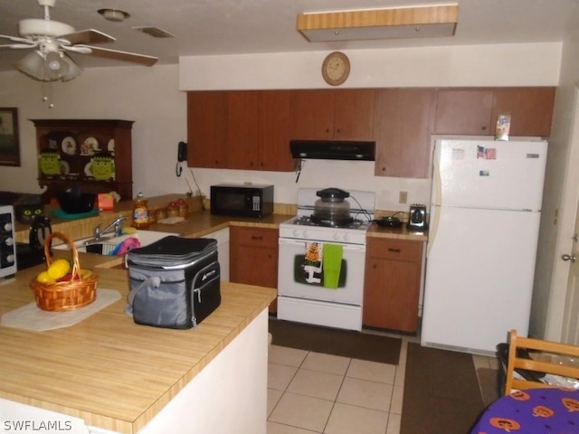 kitchen with light tile patterned floors, under cabinet range hood, white appliances, light countertops, and brown cabinetry