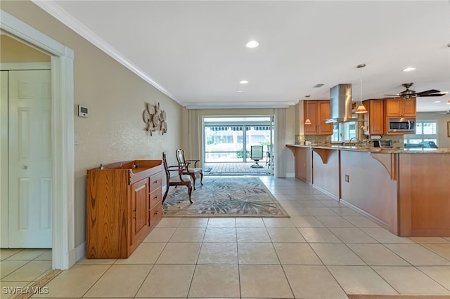 kitchen featuring light tile patterned floors, light stone counters, ceiling fan, wall chimney exhaust hood, and decorative light fixtures