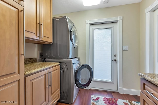 washroom with wood-type flooring, stacked washer and dryer, and cabinets