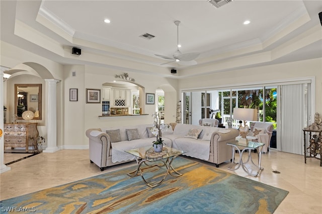 living room with a tray ceiling, ornamental molding, ceiling fan, and ornate columns