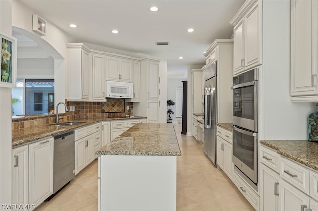 kitchen with sink, stainless steel appliances, light stone counters, white cabinets, and a kitchen island