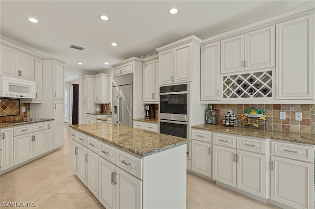 kitchen with stainless steel appliances, light stone counters, white cabinets, a kitchen island, and decorative backsplash