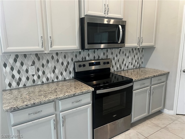 kitchen with light tile patterned flooring, appliances with stainless steel finishes, white cabinetry, backsplash, and light stone counters