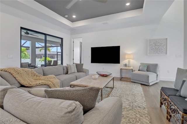 living room featuring a tray ceiling, light wood-type flooring, and ceiling fan