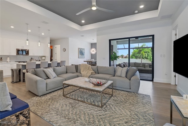 living room with light hardwood / wood-style flooring, ceiling fan with notable chandelier, and a raised ceiling