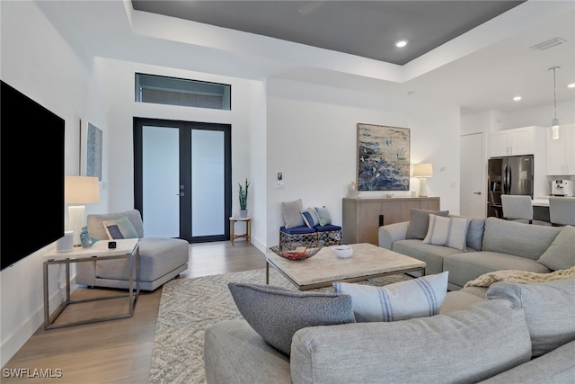 living room featuring french doors, light hardwood / wood-style flooring, and a raised ceiling