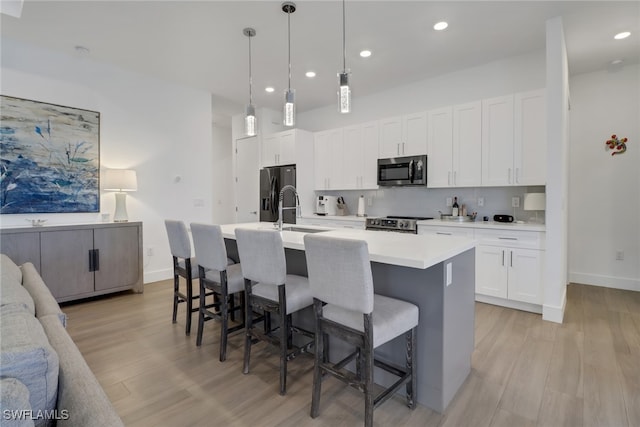 kitchen with white cabinetry, light wood-type flooring, a kitchen bar, appliances with stainless steel finishes, and a center island with sink