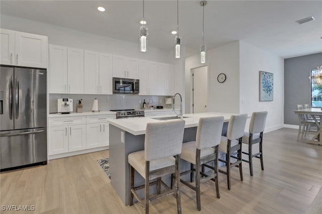 kitchen featuring light wood-type flooring, backsplash, a kitchen island with sink, appliances with stainless steel finishes, and sink