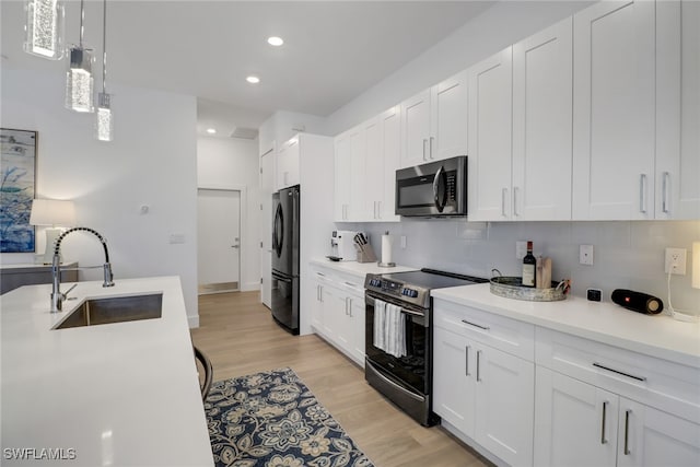 kitchen featuring appliances with stainless steel finishes, white cabinets, sink, light hardwood / wood-style floors, and decorative backsplash