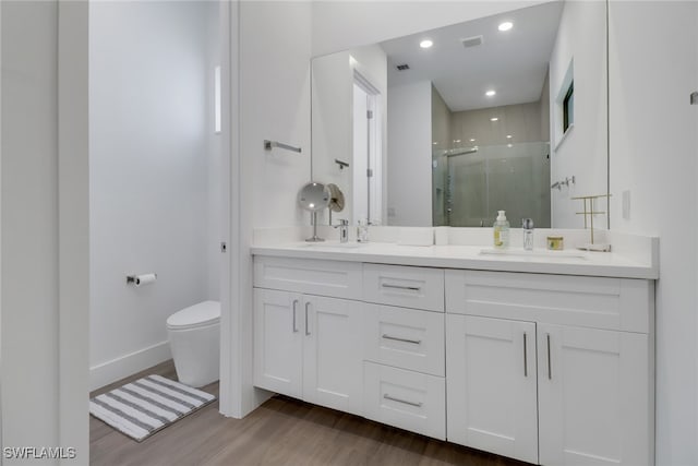 bathroom with hardwood / wood-style flooring, a shower with shower door, toilet, and dual bowl vanity