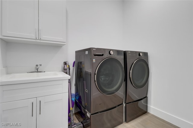 laundry area featuring light hardwood / wood-style floors, sink, cabinets, and washing machine and clothes dryer