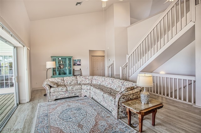 living room featuring light hardwood / wood-style flooring, ceiling fan, and a towering ceiling