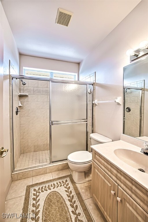 bathroom with vanity, tile patterned floors, a shower with door, and toilet