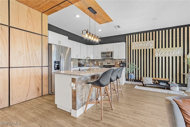 kitchen featuring stainless steel appliances, white cabinets, light stone counters, hanging light fixtures, and decorative backsplash