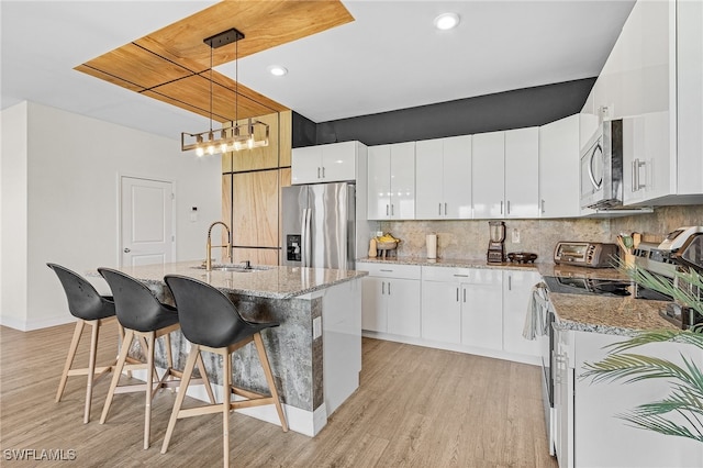 kitchen featuring white cabinetry, tasteful backsplash, stainless steel appliances, light hardwood / wood-style floors, and hanging light fixtures