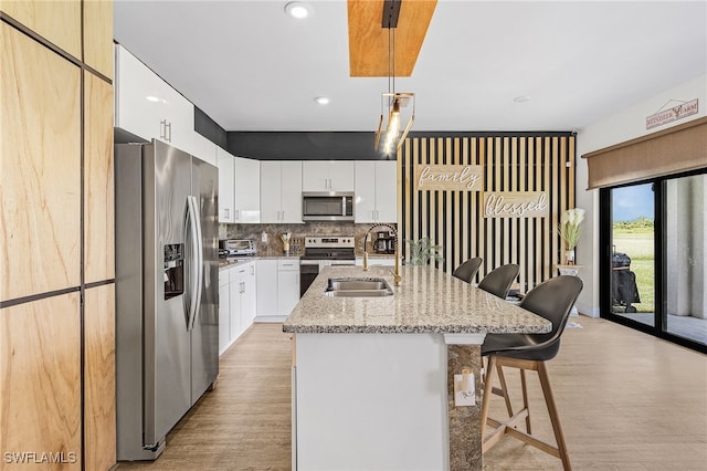 kitchen with light hardwood / wood-style flooring, white cabinets, an island with sink, hanging light fixtures, and appliances with stainless steel finishes