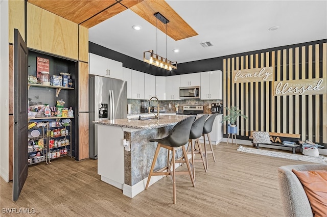 kitchen featuring decorative light fixtures, stainless steel appliances, decorative backsplash, light stone countertops, and a center island with sink