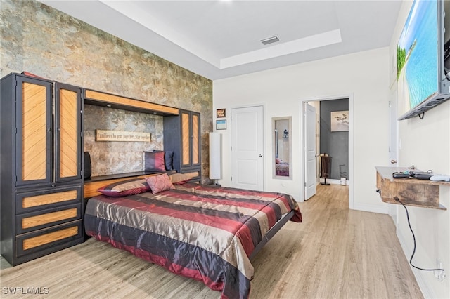 bedroom featuring light wood-type flooring and a raised ceiling