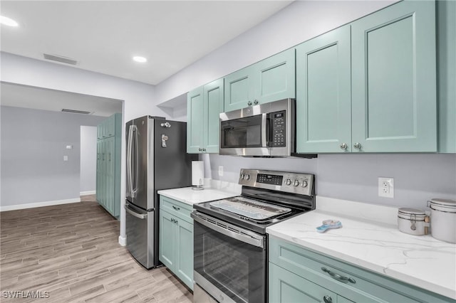 kitchen featuring appliances with stainless steel finishes, green cabinets, light stone counters, and light hardwood / wood-style flooring