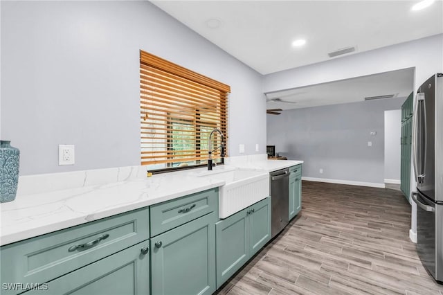 kitchen with sink, light wood-type flooring, green cabinets, stainless steel appliances, and light stone countertops