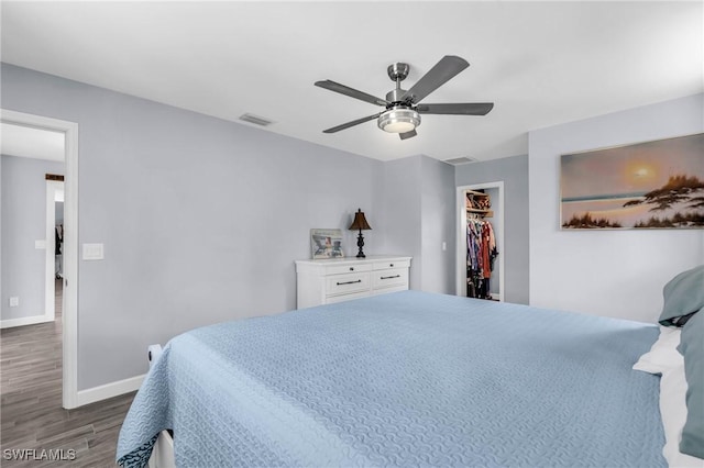 bedroom with a closet, a spacious closet, dark hardwood / wood-style floors, and ceiling fan