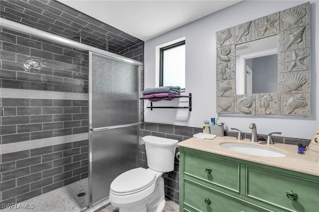 bathroom with vanity, a shower with door, tile walls, and toilet