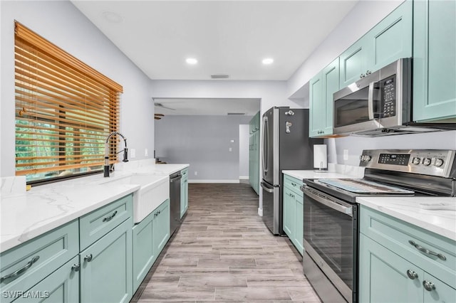 kitchen featuring sink, green cabinetry, light hardwood / wood-style flooring, appliances with stainless steel finishes, and light stone countertops