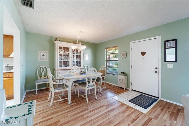 dining room with a chandelier, light hardwood / wood-style floors, and a textured ceiling