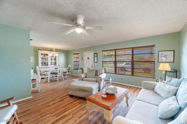 living room featuring ceiling fan with notable chandelier, a textured ceiling, and light hardwood / wood-style floors