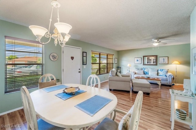 dining space with a textured ceiling, ceiling fan with notable chandelier, and wood-type flooring