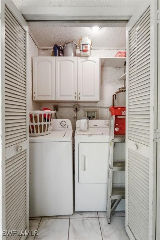 clothes washing area with light tile patterned floors, washing machine and dryer, a textured ceiling, and cabinets