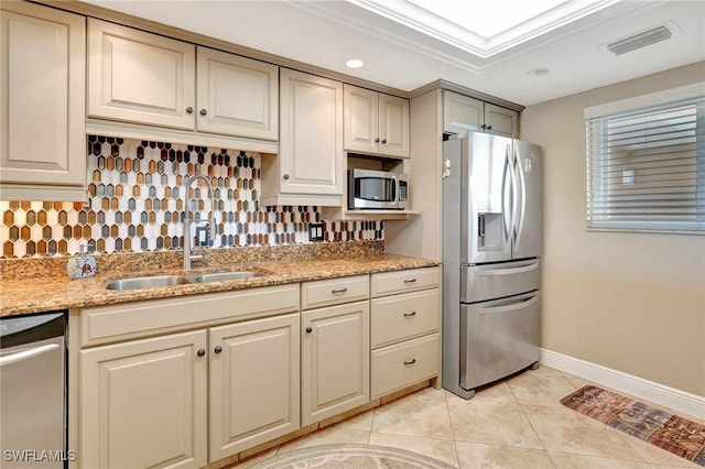 kitchen with tasteful backsplash, light tile patterned floors, stainless steel appliances, light stone countertops, and cream cabinetry